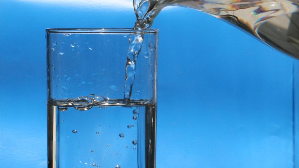 Foto toont het inschenken van water in een glas vanuit een glazen kan